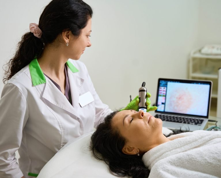 Clinic employee performs a diagnostic procedure for a patient using a modern dermatoscope, the image is displayed on the monitor